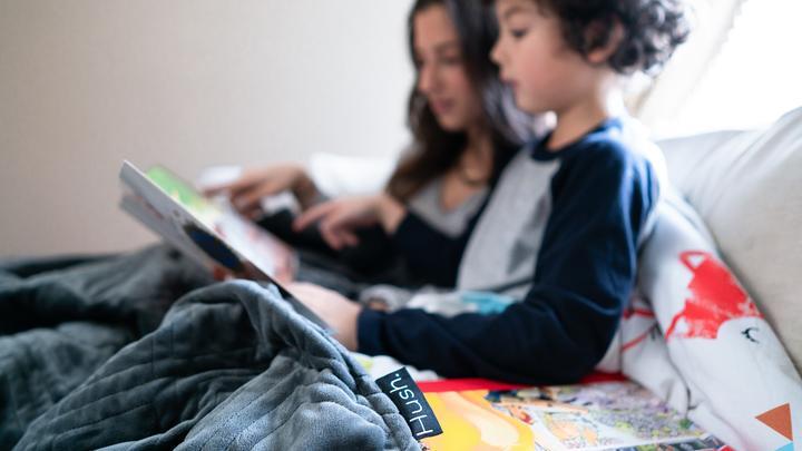 little boy and a woman reading a book under a Hush children's weighted blanket