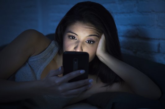 sleep procrastination: Woman looking at her phone while in bed