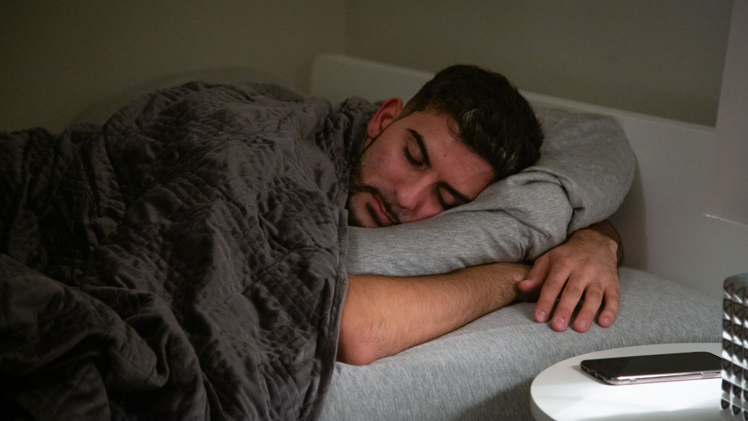 A man hugging his pillow while cozy sleeping in prone position under a Hush Classic Weighted Blanket.