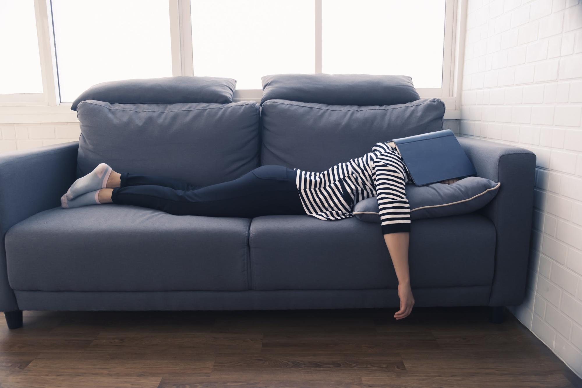 sleep latency: Woman lying face down on a couch with a book covering her head