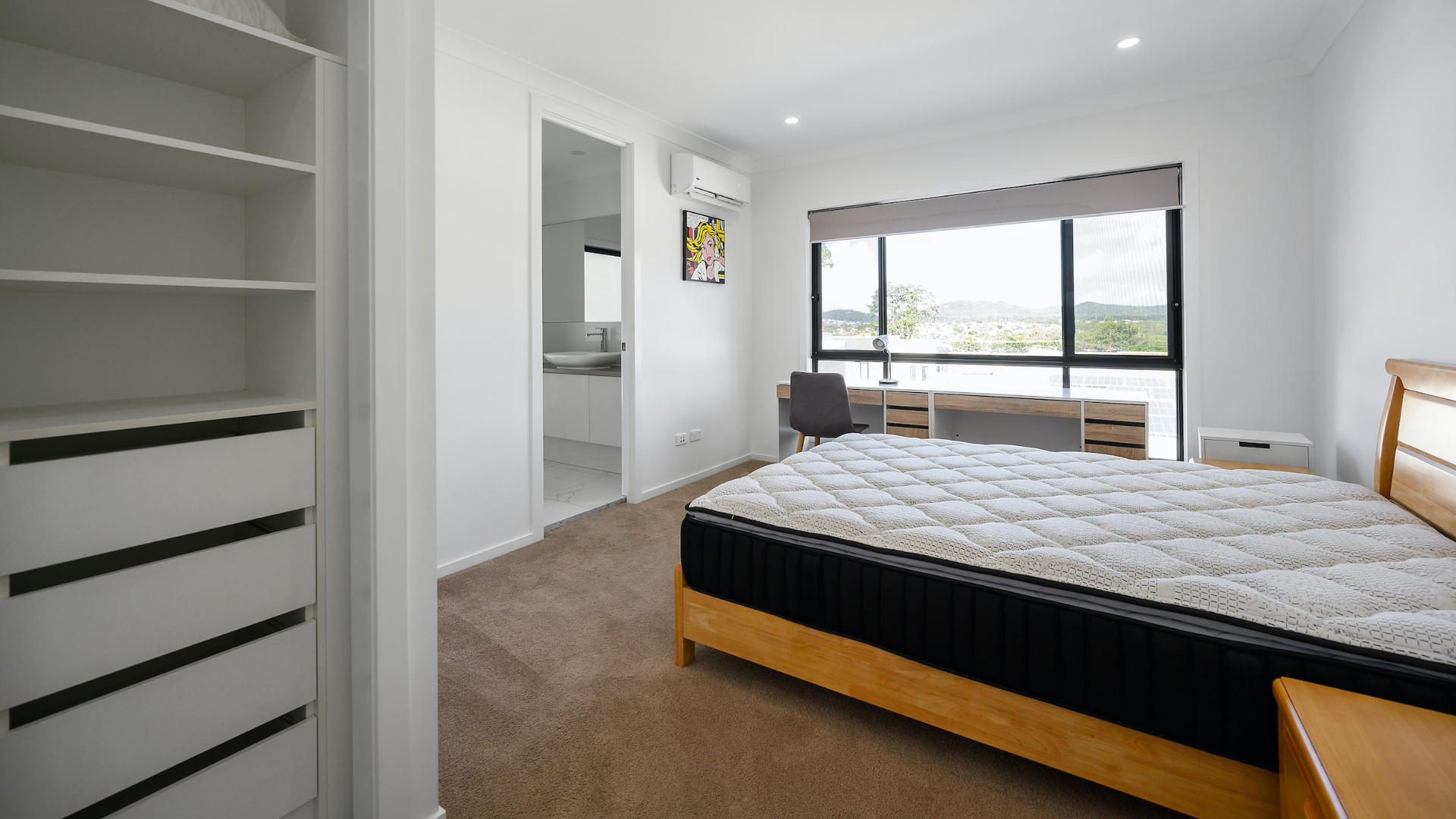 A well-lit bedroom with a new mattress on the bed and empty shelves on the left side.