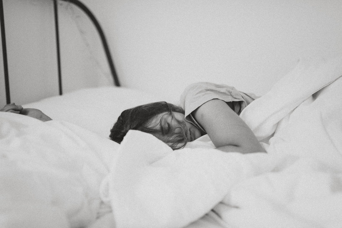 A grayscale photo of a sleeping woman lying in bed and tucked in a white blanket