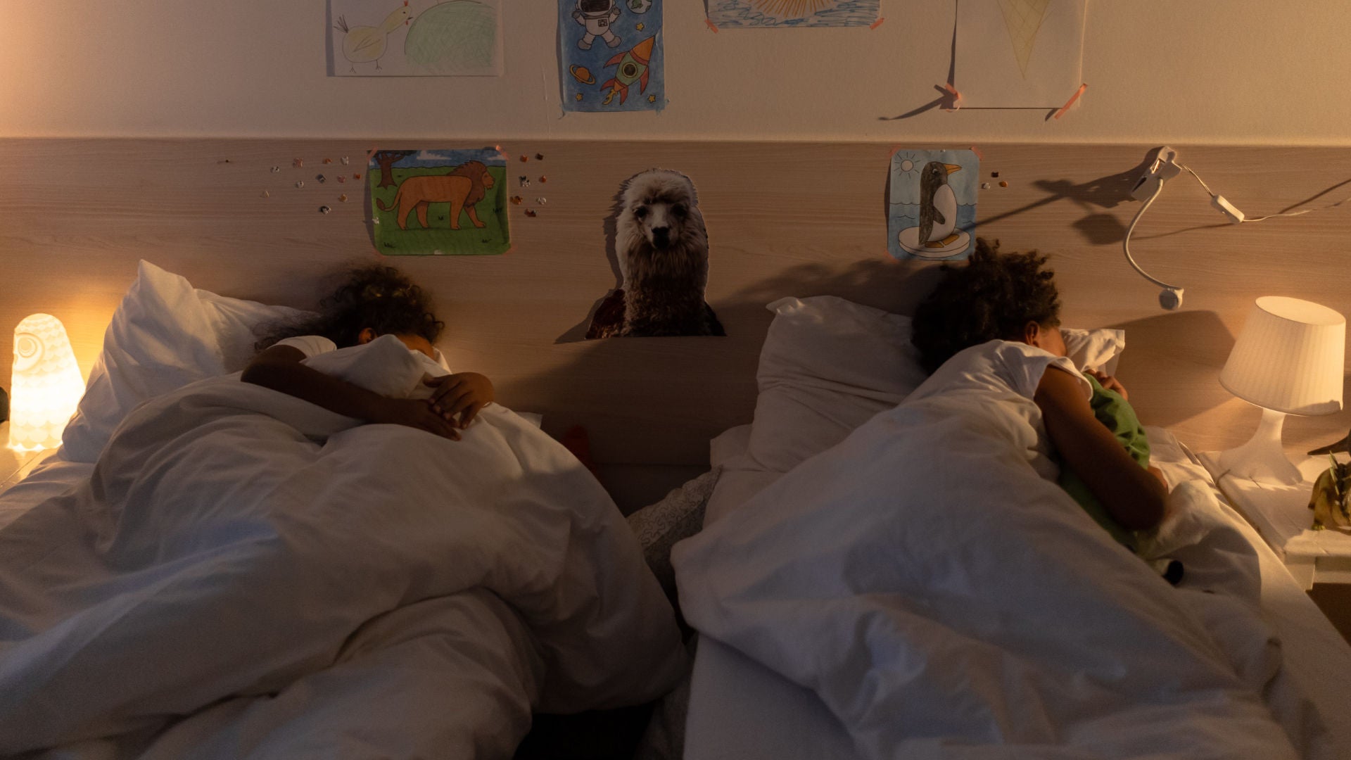 Two children sharing a room and sleeping on their beds with night lamps on each side.