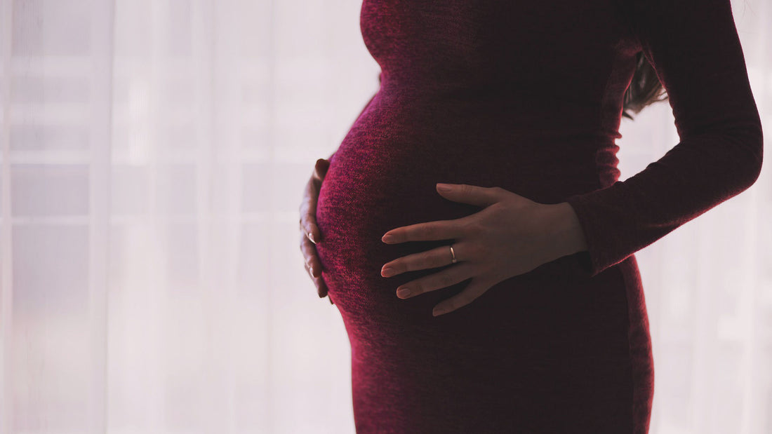 A pregnant woman wearing a dark red dress holds her belly.