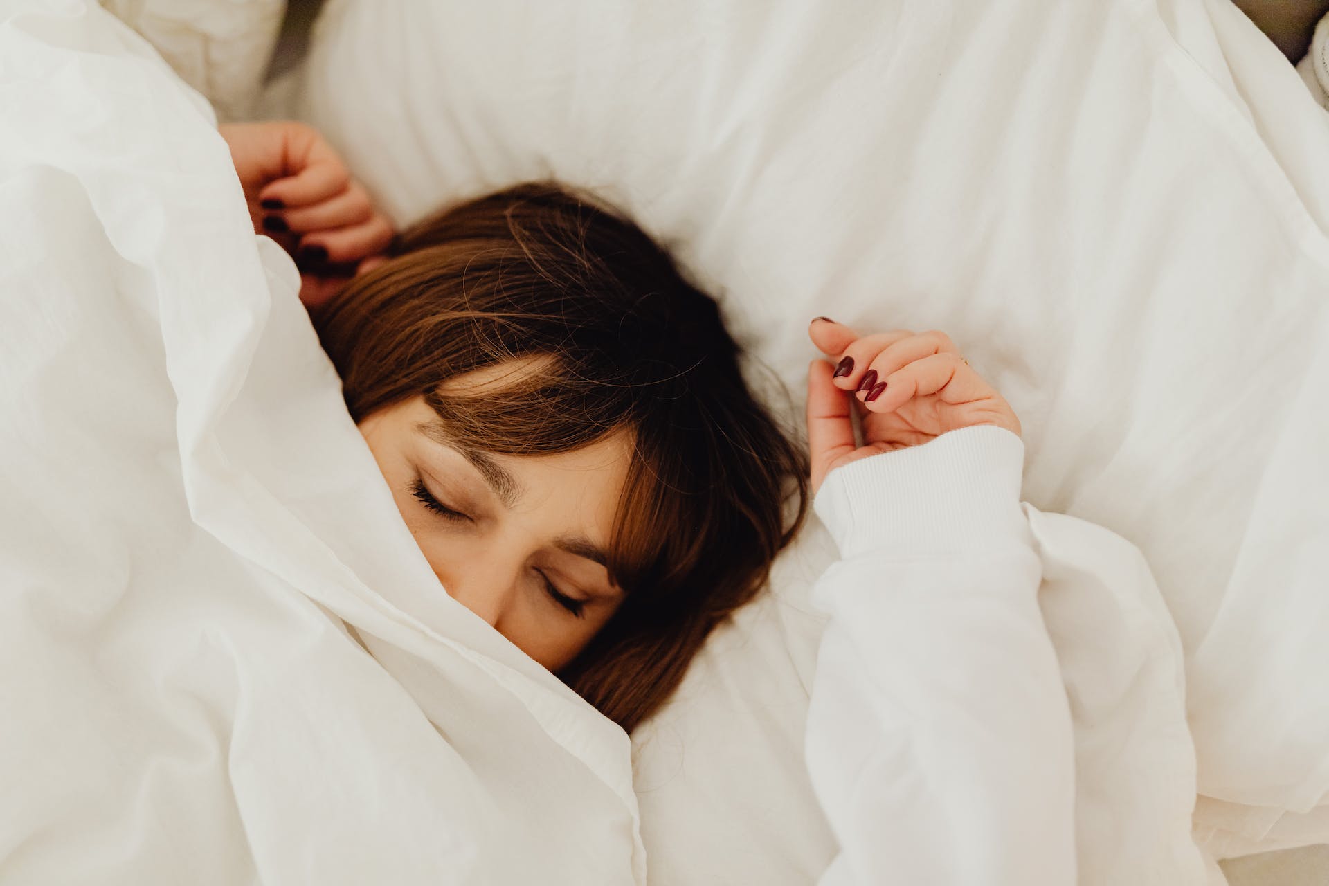 a woman sleeping on a white bed covered in white sheets